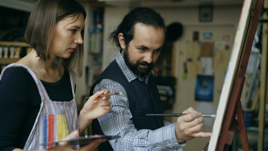 Artist teaching student painting on easel in studio