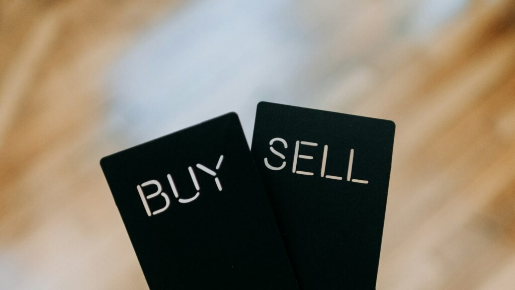 A hand holding two black cards with the words buy and sell written on them