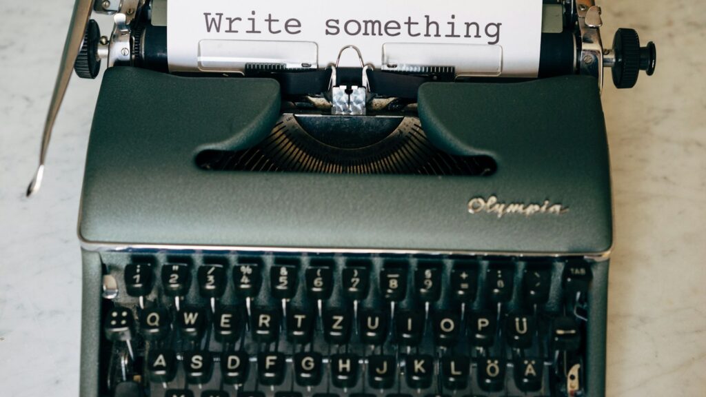 An Olympia typewriter with paper reading "Write something" on a marble surface