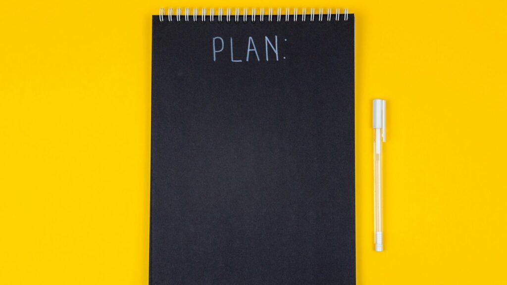 A black spiral notebook with the word PLAN written on a yellow background