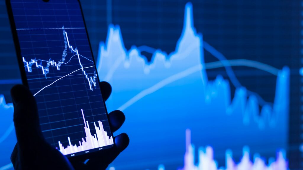 A person holding a cell phone in front of a stock chart
