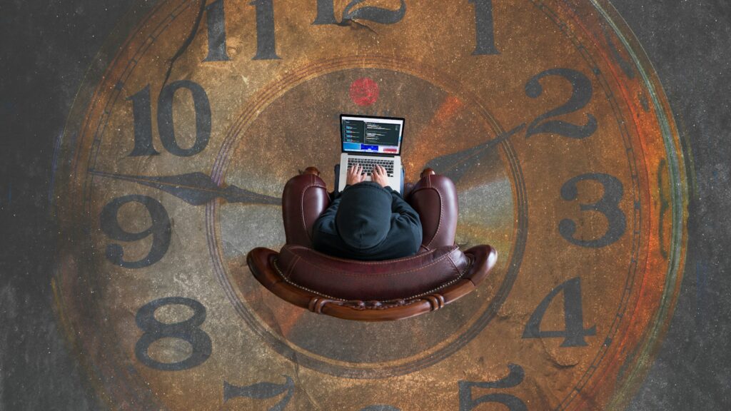 A person in a hoodie typing on a laptop in a leather armchair