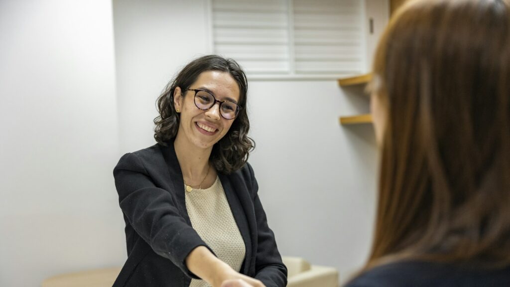 A woman shaking hands with another woman sitting at a table