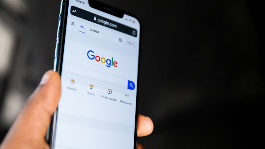 A hand holding a smartphone displaying the Google search engine homepage