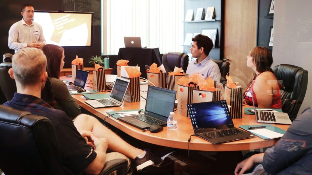 Man standing in front of people sitting beside table with laptop computers