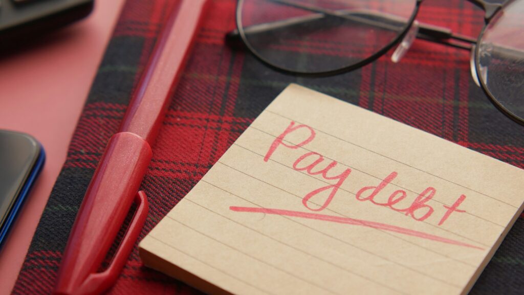 A note that says pay debt next to a pen and glasses