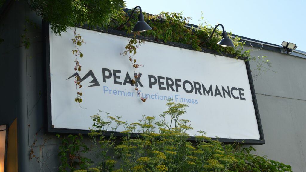 A white 'peak performance' sign surrounded by green foliage