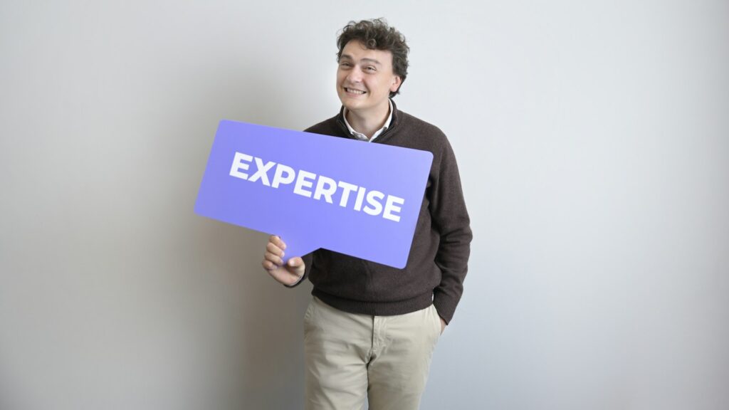 Smiling man holds a purple "expertise" sign