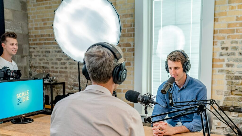 Two men wearing headphones recording a podcast at a wooden table in a studio
