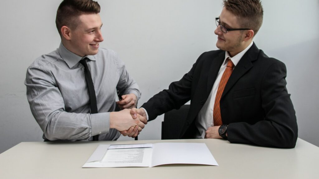 Two men facing each other while shake hands and smiling