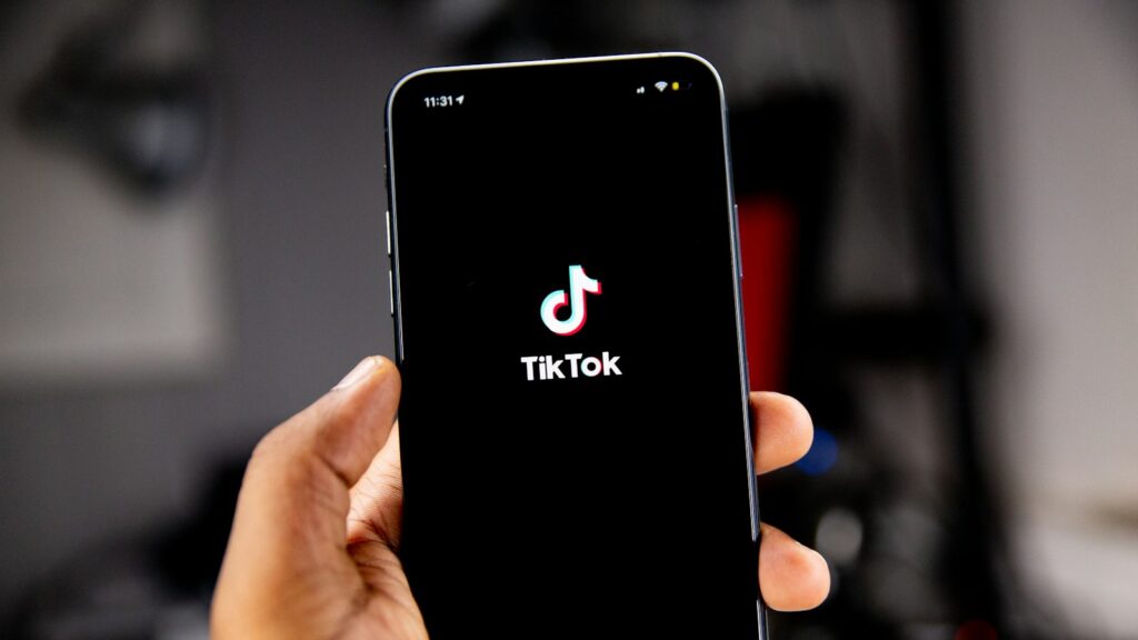 A hand holding a smartphone displaying the TikTok logo on a black screen