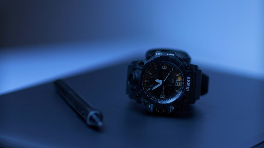 A black wristwatch and pen on a dark surface