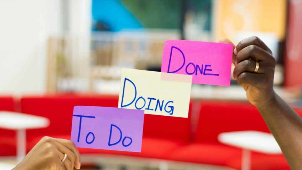 Hands holding three sticky notes labeled To Do, Doing, and Done in a workspace