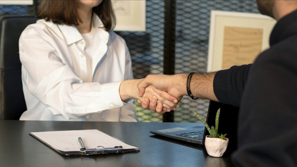 A man and a woman shaking hands in front of a laptop