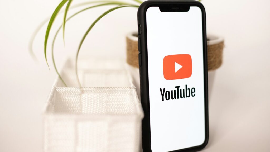 A phone with a youtube logo on it next to a potted plant